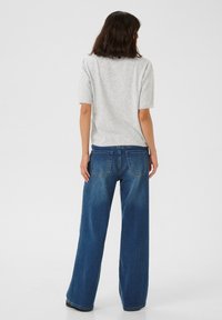 Un pull gris clair à manches courtes associé à un jean en denim bleu ample. Le jean possède deux poches arrière et une coupe droite et large.