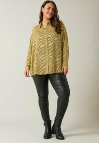 Long-sleeve, button-up shirt in olive green with a wavy pattern, paired with fitted black faux leather pants and ankle boots.