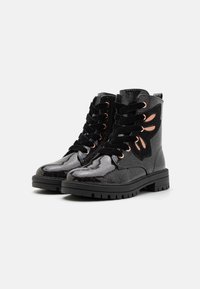 Botines negros brillantes con una superficie lisa, cordones negros y ojales en oro rosa; presenta detalles decorativos de ante negro.