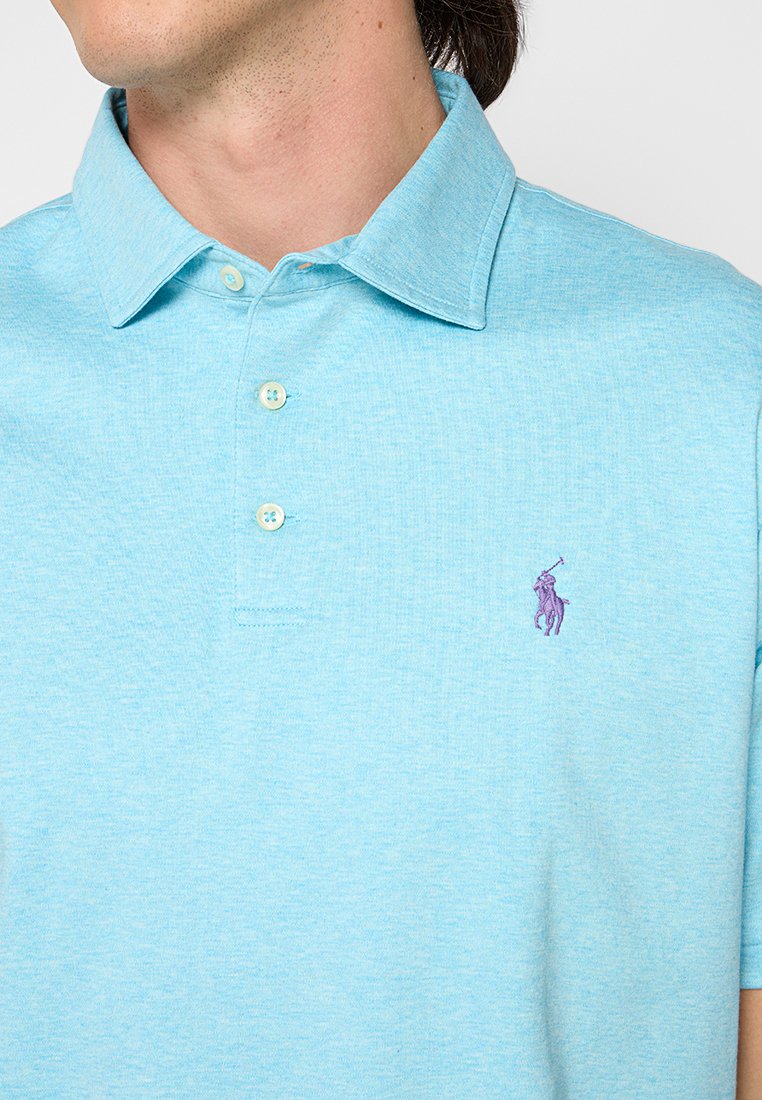 Jasnoniebieska koszulka polo wykonana z miękkiego, teksturowanego materiału. Posiada kołnierzyk zapinany na trzy guziki oraz małe, fioletowe haftowane logo na piersi.