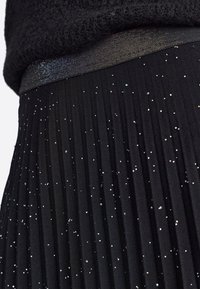 Jupe plissée noire avec une ceinture texturée, ornée d'accents argentés et iridescents dispersés sur le tissu.