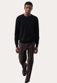 Pull en maille noir associé à un pantalon marron cintré. Le pull a un col rond et des manches longues ; le pantalon a une coupe droite.