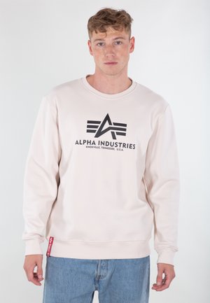 Lys beige sweatshirt lavet af bomuldsblanding, med et sort logo og trekantet design på forsiden. Ribbet manchetter og kant. Blå jeans brugt.