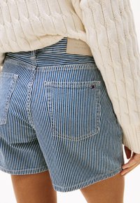Pantalones cortos de mezclilla con rayas azules y blancas, de cintura alta, con dos bolsillos traseros y una pequeña etiqueta de logo en la cinturilla.