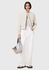 Chaqueta bomber beige claro, camiseta blanca, pantalones anchos blancos, bolso metálico plateado y sandalias negras con acentos plateados.