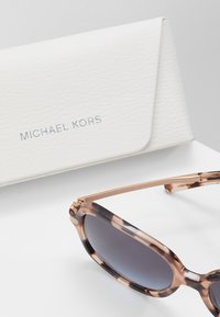 Ochelari de soare Michael Kors cu ramă din fivă țestoasă, lentile întunecate și accente din metal auriu, însoțiți de un etui alb texturat.