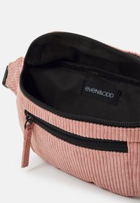 Marsupio in corduroy rosa con cerniera nera e interno coordinato. Presenta una finitura testurizzata e una piccola tasca esterna con linguetta per il tiraggio.