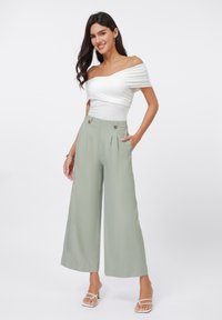 Off-the-shoulder white top paired with wide-leg, light green trousers featuring front pleats and dual button accents. Smooth fabric texture.