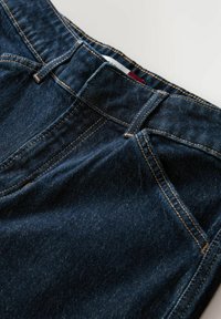 Sötétkék farmernadrág látható varrással, hagyományos ötpocketes kialakítással és enyhén texturált felülettel a derékrész közelében.