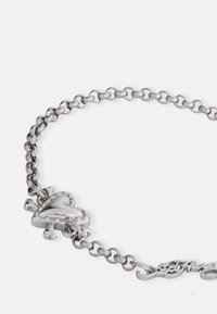 Sølvmetallarmbånd med et hjerteformet anheng og et dekorativt skrifttypeakcent. Kjedeforbindelsesdesign med polert overflate og glitrende tekstur.