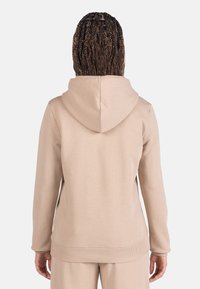 Sudadera con capucha beige de textura suave, con puños y dobladillo acanalados. Presenta un ajuste relajado y una capucha con cordón ajustable.
