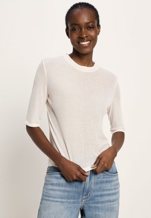 Leichtes, geripptes weißes T-Shirt mit Rundhalsausschnitt und kurzen Ärmeln, kombiniert mit blauen Jeans, die eine entspannte Passform und glatte Textur zeigen.