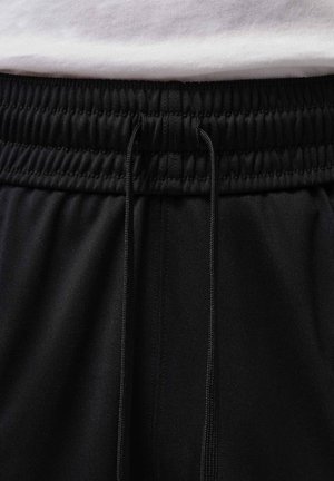 Schwarzer elastischer Bund mit Kordelzug an schwarzen Hosen, kombiniert mit einem weißen, hineingesteckten Hemd.