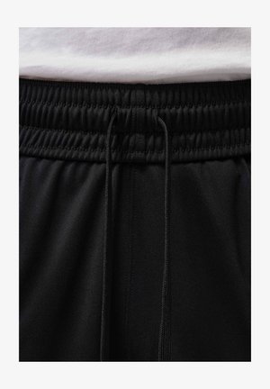 Cintura elástica negra con cordones en pantalones negros, combinados con una camisa blanca metida.