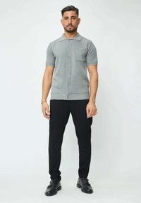 Pull à manches courtes gris avec boutons et poche, associé à un pantalon slim noir et des chaussures noires. Texture lisse et design ajusté.