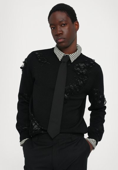 Pull noir avec des accents en dentelle texturée, associé à une chemise à carreaux et une cravate noire. Tissu en maille lisse, coupe classique, design minimaliste.