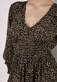 Kleid im Leopardenmuster in Grün und Beige, mit tiefem V-Ausschnitt, langen Ärmeln, elastischem Rüschenbund an der Taille und einem fließenden Rock.