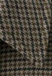 Gros plan sur un tissu en laine texturé avec un motif pied-de-poule dans des tons marron, beige et noir, montrant des couches pliées.