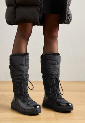 Knæhøje sorte pufferstøvler med fake fur kant, skinnende vandtæt overdel, tekstureret sål og justerbar snøre detaljer.