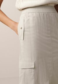 Jupe cargo grise claire avec une taille élastique, dotée d'une poche latérale et d'un tissu texturé avec un éclat subtil.