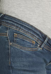 Blå denimjeans med nærbillede af taljen, kontrasterende orange syninger og en lille detalje med en forlommes.