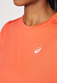 Short-sleeve, crew-neck athletic shirt in bright orange fabric with a smooth texture, featuring a white logo on the left chest.