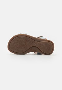 Bruine rubberen zool met een gestructureerd bloemdesign, voorzien van blauwe textiele banden met verstelbare hardware voor een veilige pasvorm.