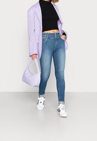 Ljuslila oversize blazer, svart ribbad cropped topp, blå skinny jeans, vita sneakers med svarta accenter, och matchande ljuslila handväska.