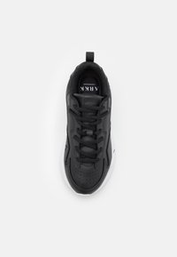 Černá sportovní bota s texturovaným koženým svrškem, perforovanými detaily a bílou podrážkou. Má černé tkaničky a zadní poutko pro snadné oblékání.