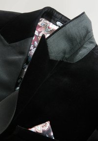 Schwarzer Samtblazer mit Satin-Revers, ausgestattet mit einem gemusterten Seiden-Einstecktuch und einem blumigen Futter in Burgunder- und Blautönen.