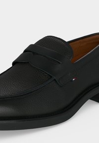 Μαύρο ανδρικό παπούτσι loafer από δέρμα με λείο λουράκι μπροστά και μικρό υφασμάτινο λογότυπο κοντά στη πλευρική ραφή.