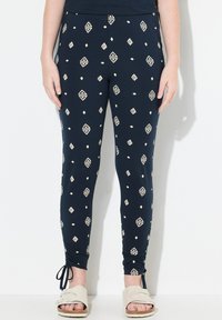 Granatowe legginsy wykonane z elastycznego materiału, zdobione geometrycznym kremowym wzorem, o dopasowanym kroju i ściąganych kostkach z wiązaniami.