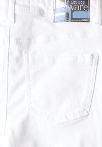 Jeans de denim blanco con un bolsillo trasero, costuras visibles y una etiqueta de tela con un diseño en azul y negro.