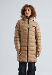 Tan pufferjas met horizontale stiksels, een ritsluiting, zijzakken en een capuchon. Zwarte accenten op de rits en het logo op de borst.