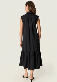 Vestido negro sin mangas con un dobladillo rizado, un corpiño fruncido y cuello. Diseñado en una tela ligera con una textura suave.