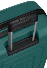 Valise rigide verte avec une poignée rétractable noire déployée et une fermeture éclair noire visible sur le bord supérieur.