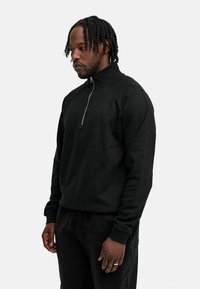 Black fleece quarter-zip sweatshirt with a high collar, ribbed cuffs, and relaxed fit. Fabric appears soft with a smooth texture.