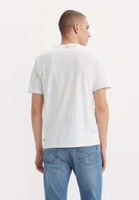 Witte katoenen T-shirt met korte mouwen en een ronde halslijn, gecombineerd met lichtblauwe jeans met achterzakken. Eenvoudig en klassiek ontwerp.