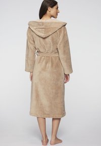 Beige morgonrock med huva, tillverkad av mjukt, texturerat tyg, med ett knytband i midjan och långa ärmar, som sträcker sig till halvkalvslängd.