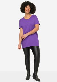 Paarse tuniekshirt met korte mouwen, ronde hals en een ontspannen pasvorm, gecombineerd met glanzende zwarte leggings en gestudden zwarte enkellaarzen.