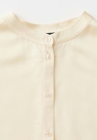 Hemd in Cremefarbe mit Stehkragen und vier kleinen, runden Knöpfen in der vorderen Mitte.