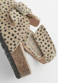 Beige Wildledersandale mit schwarzen Spitzen, zwei verstellbaren Riemen und einer strukturierten braunen Kork-ähnlichen Sohle. Verfügt über eine dunkle Gummisohle für besseren Halt.