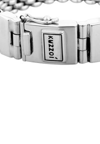 Silverfärgad metallarmband med länkdesign. Har ett lås med varumärket "Kuzzoi" på en rektangulär platta. Slät yta.