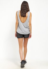 Szary bezrękawnik z głębokim dekoltem na plecach, zestawiony z czarnymi szortami. Charakteryzuje się luźnym krojem i miękką teksturą. Obuwie to czarne buty sportowe.