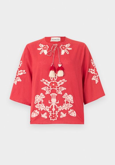 Blouse rouge avec broderie florale blanche sur le devant et les manches, dotée d'un col rond avec des cordons à pompons noués.