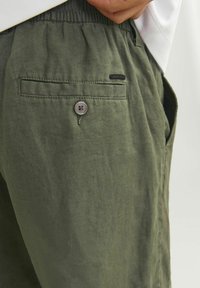 Olivgröna linnen shorts med elastisk midja, sidofickor och en bakficka med en grå knapp och en liten märkesetikett.