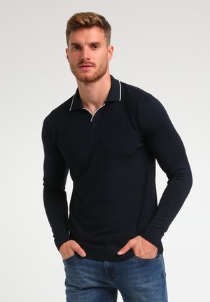 Polo de manga larga azul marino con textura acanalada, ribete blanco en el cuello y diseño ajustado. Combinado con jeans de mezclilla azules.