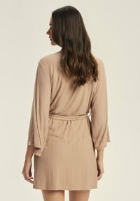 Beżowy, prążkowany szlafrok z rozkloszowanymi rękawami, paskiem w talii i długości do kolan. Miękka faktura i subtelny połysk podkreślają jego wygląd.