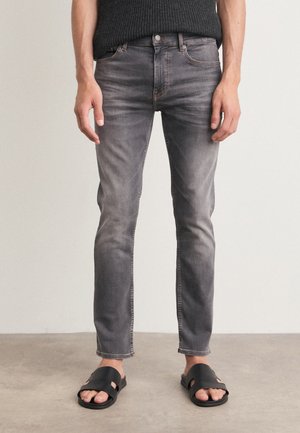 Jeans in denim grigio con vestibilità slim, caratterizzati da un motivo sbiadito, tasche frontali e chiusura a bottone. Abbinati a sandali neri a scivolo.