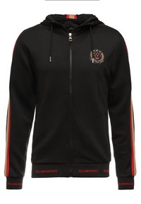 Černá mikina s kapucí na zip s červenými a béžovými pruhy na rukávech, vyšívaným znakem na hrudi a červeným nápisem "GLORIOUS" na manžetách a lemu.